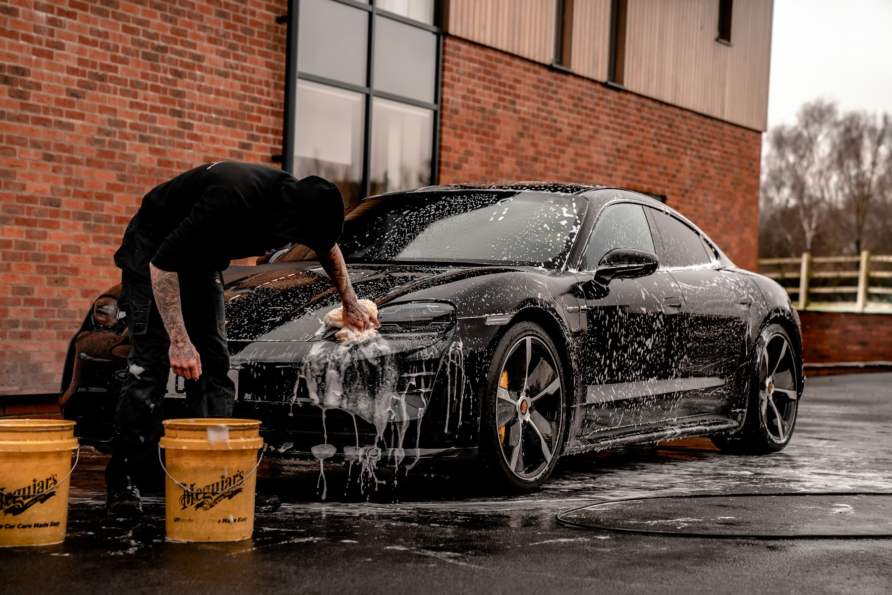 Professional detailer hand washing a luxury black vehicle